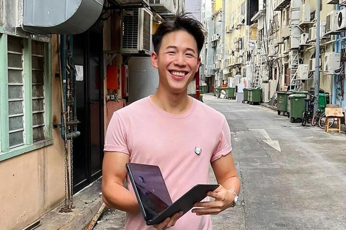 muž v růžovém tričku držící notebook