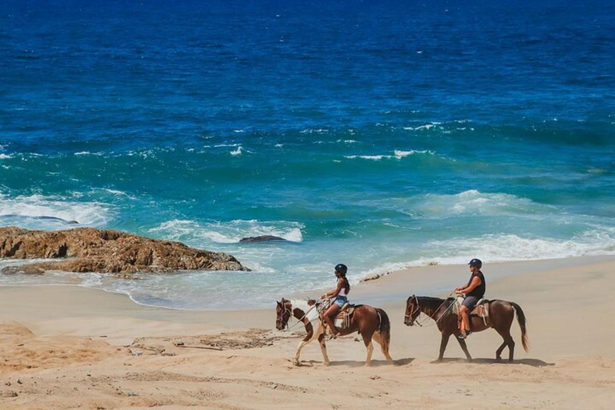 Dos personas están montando a caballo en la playa.