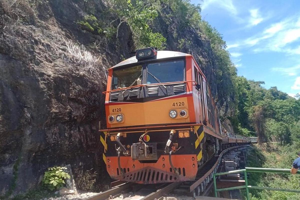 Un tren taronja és a les vies prop d'una muntanya