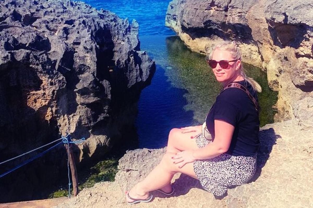 una donna seduta su una scogliera accanto a uno specchio d'acqua