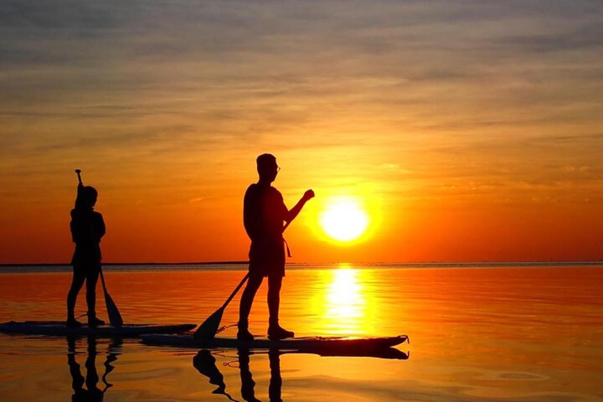 dva lidé stojící na paddleboardu ve vodě při západu slunce
