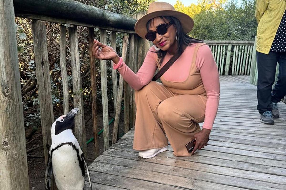 une femme accroupie sur un pont en bois nourrissant un pingouin