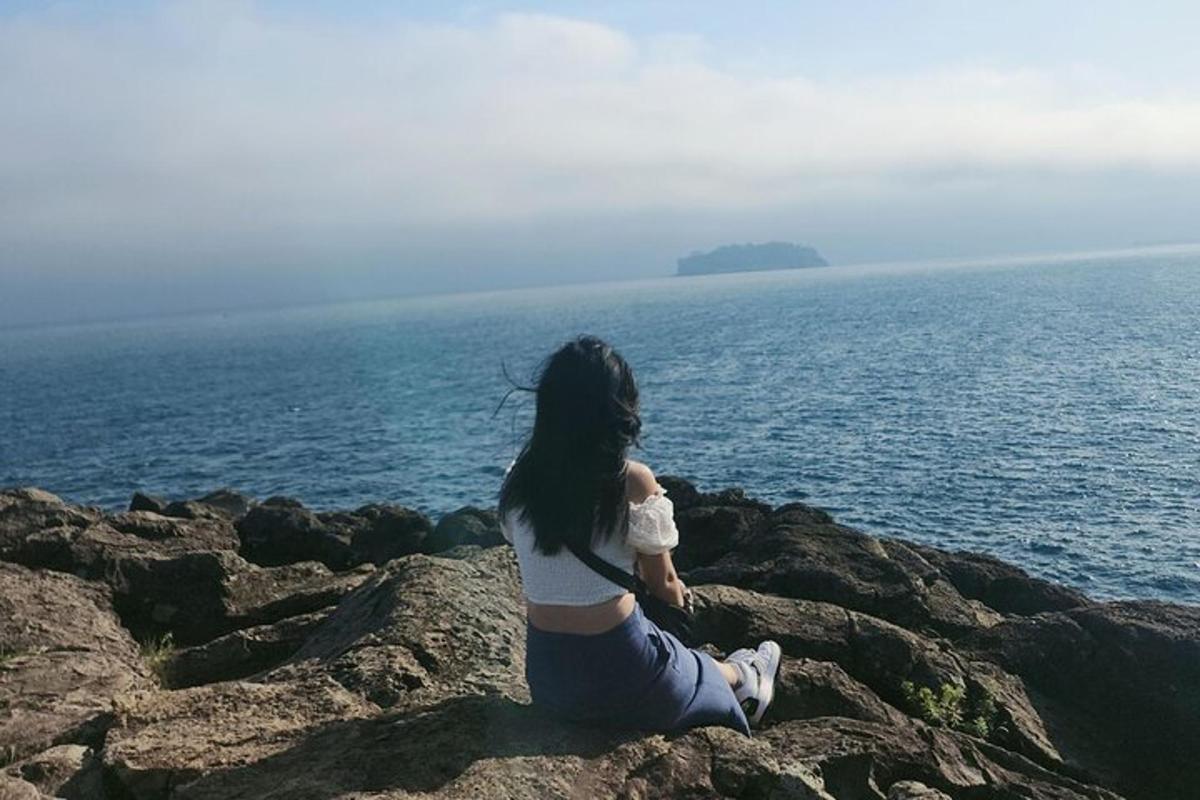 a woman sitting on a rock by the ocean