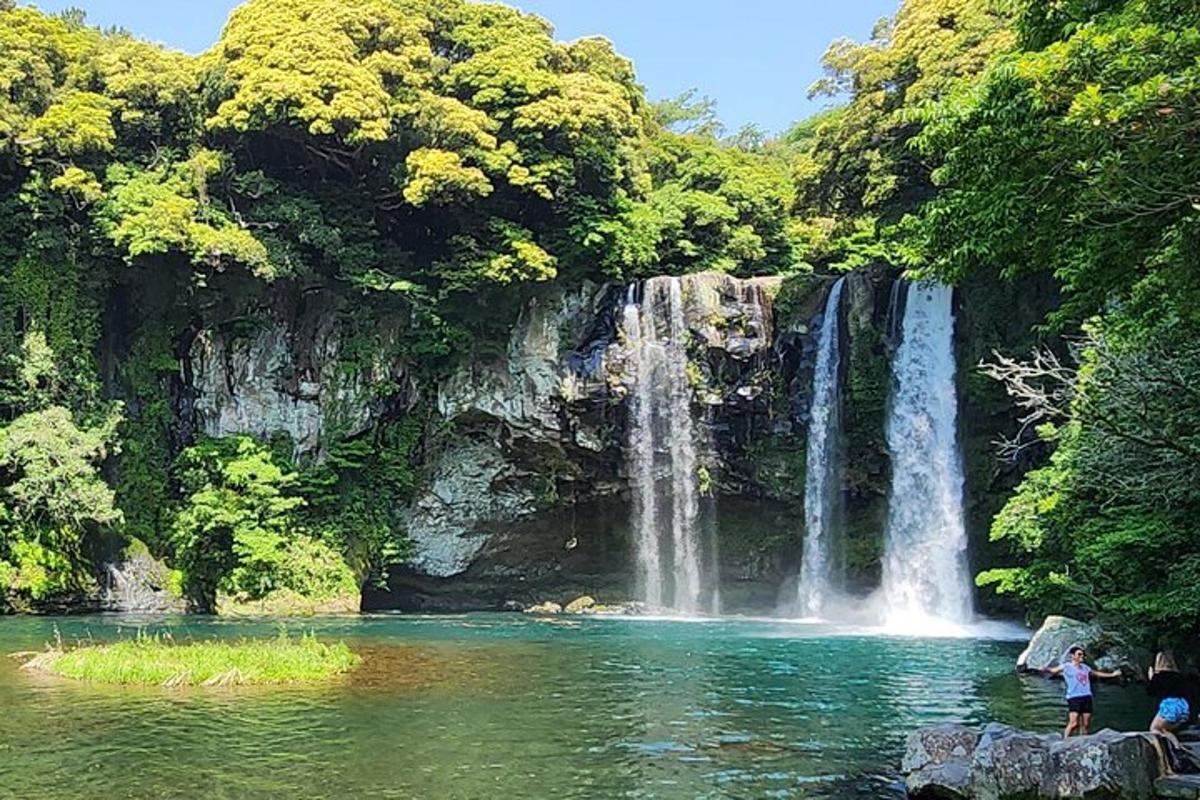a waterfall in the middle of a lake with people standing in front
