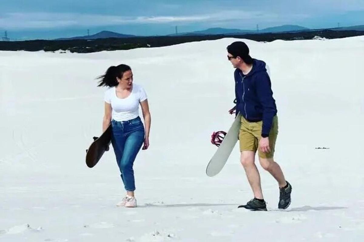 en mann og en kvinne som går på sanden med et surfebrett