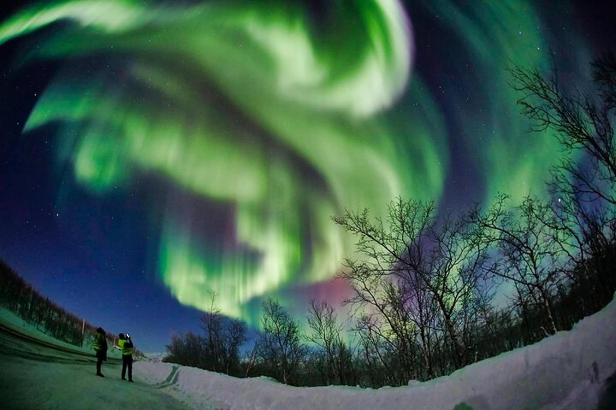 Dos personas paradas en la nieve observando la aurora boreal