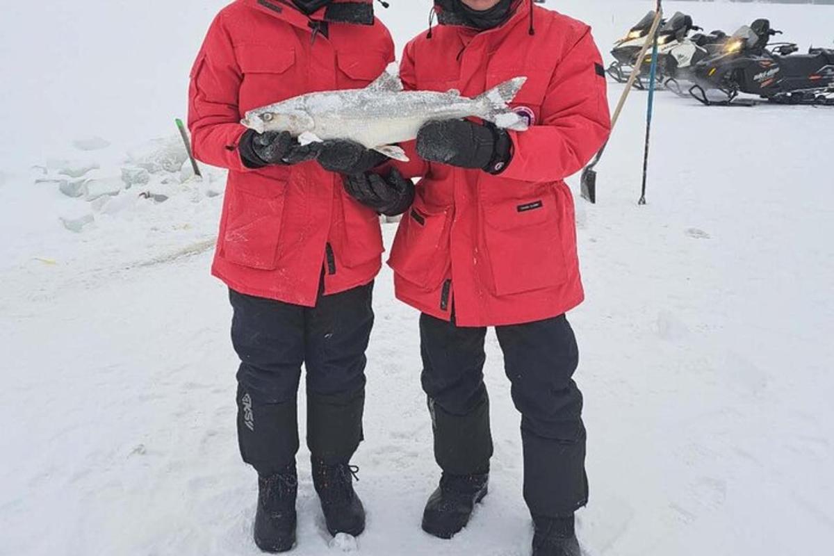 two people standing in the snow holding a fish