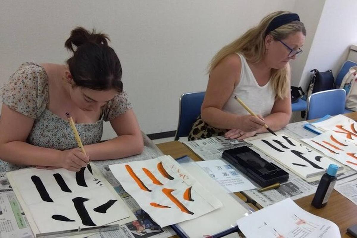 dwie kobiety siedzące przy stole i pracujące nad dziełem sztuki