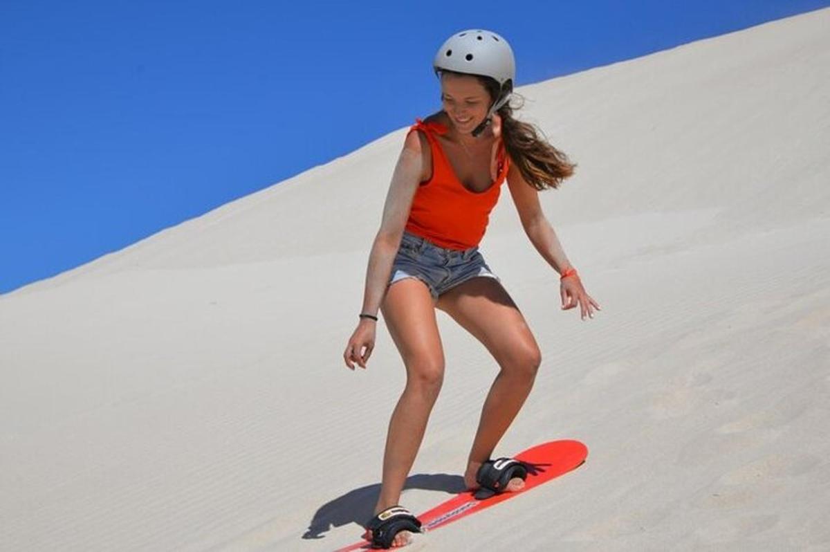 isang kabataang babae na nakasakay sa snowboard pababa sa burol ng buhangin