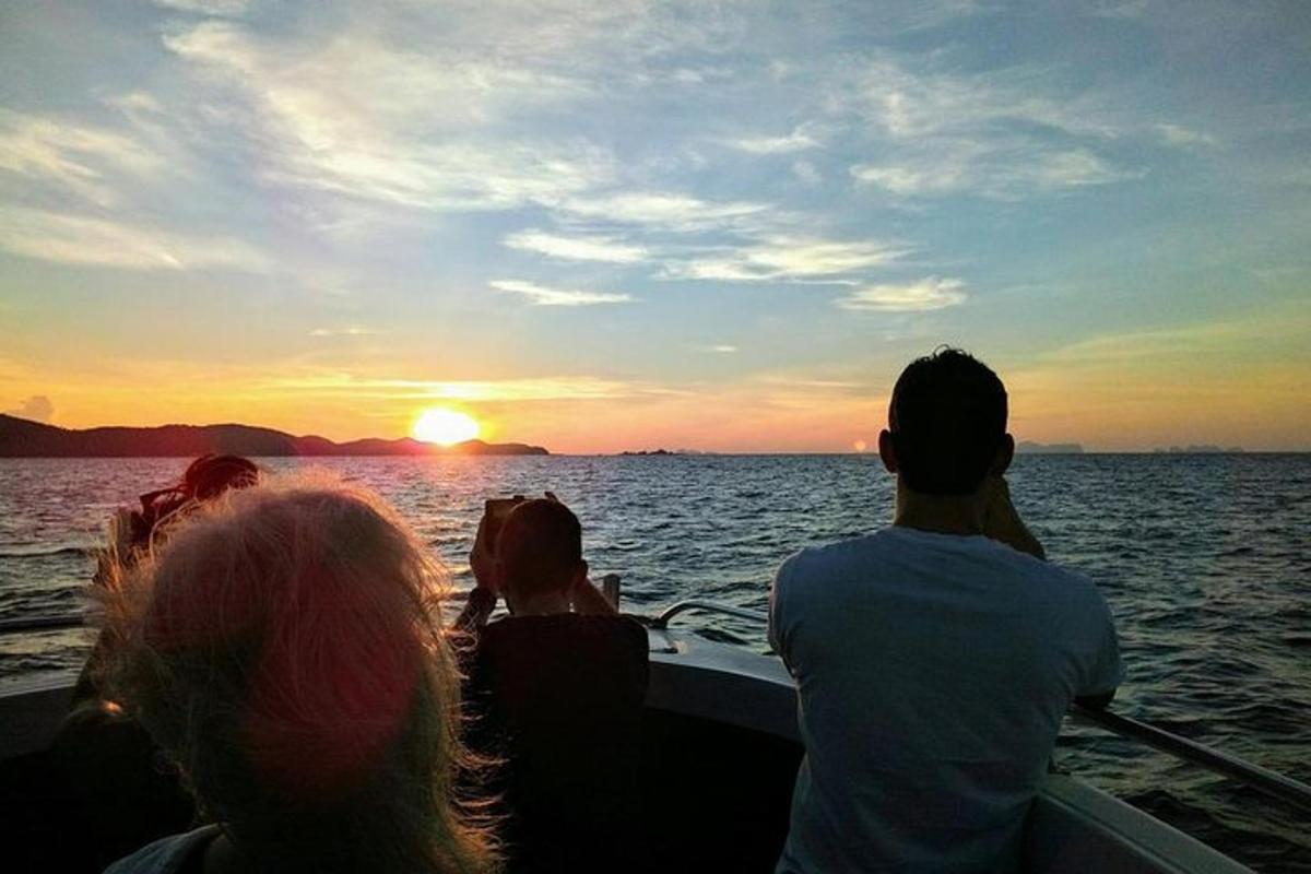 un groupe de personnes sur un bateau dans l'eau au coucher du soleil