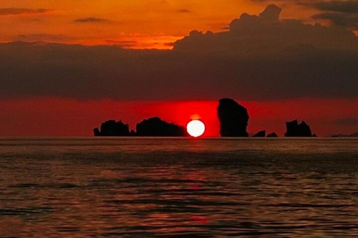 un coucher de soleil sur l'océan avec des rochers en arrière-plan