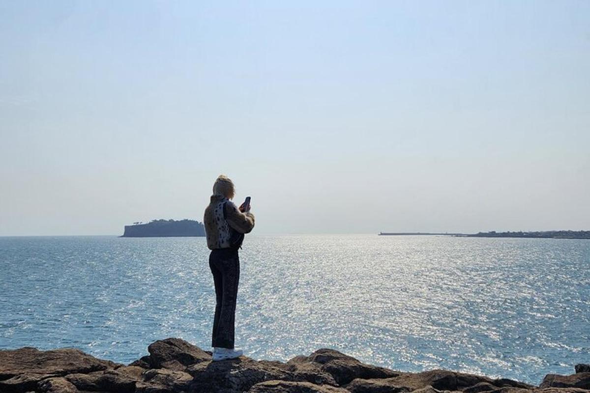 en person som står på en stein og tar et bilde av havet