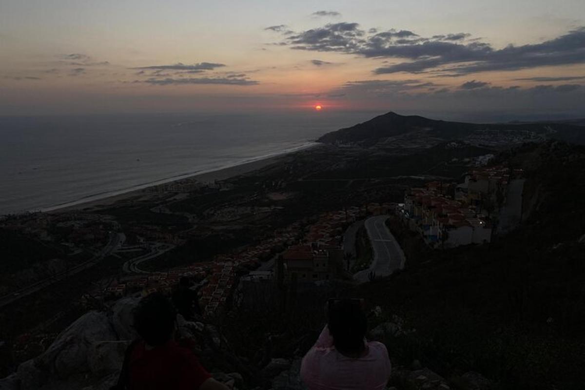 eine Gruppe von Menschen sitzt auf einem Berg und beobachtet den Sonnenuntergang