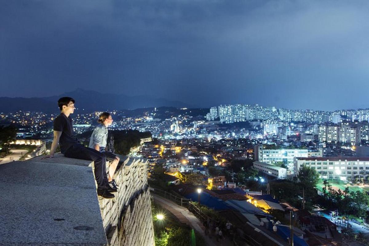 two young men sitting on the edge of a building at night