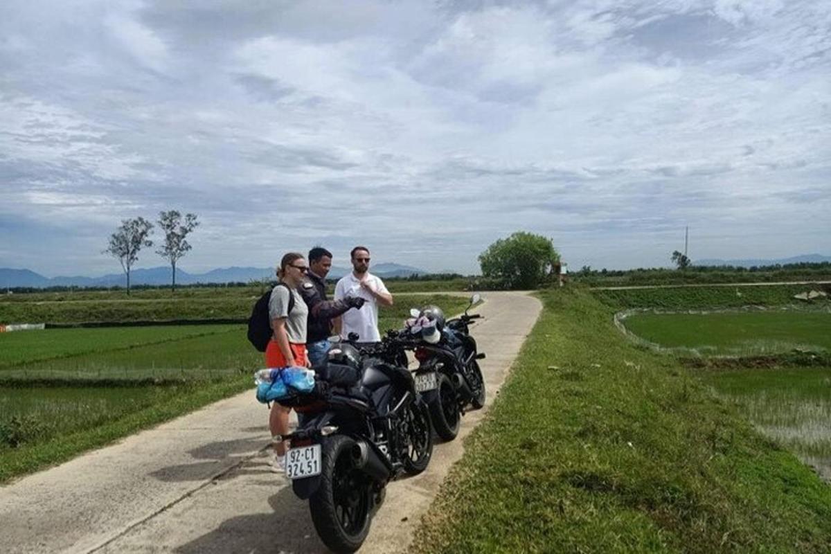 Tres hombres de pie junto a una motocicleta en una carretera