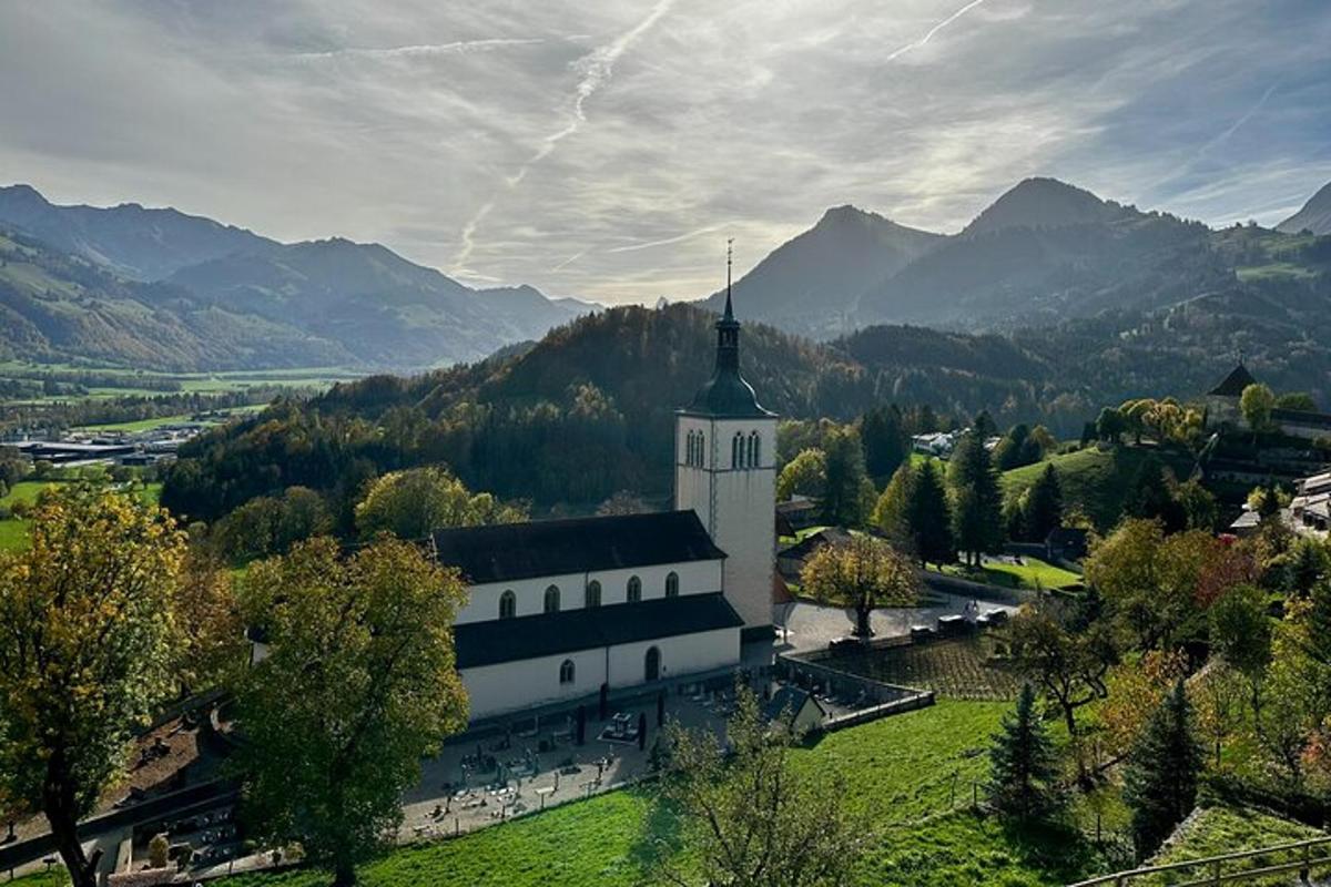 Un gran edificio blanco con un campanario en una colina con montañas.