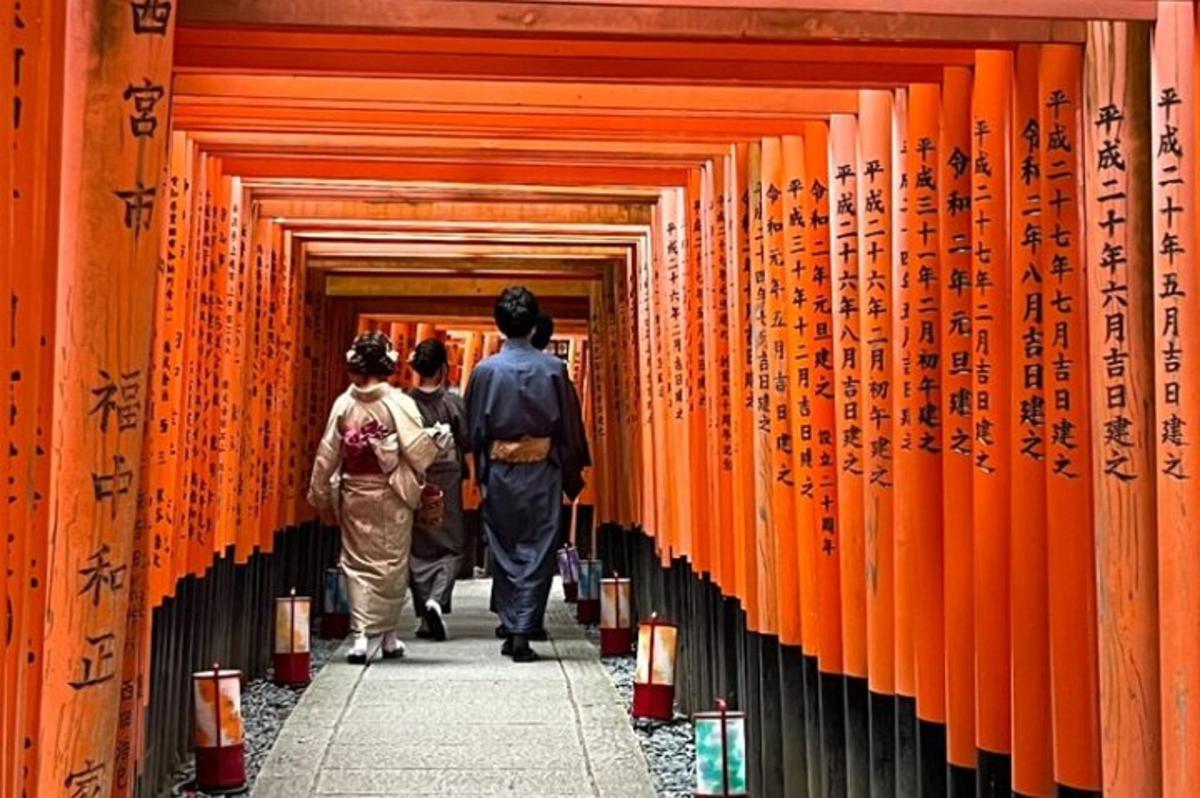 Gente caminando por un pasillo de puertas torii naranjas