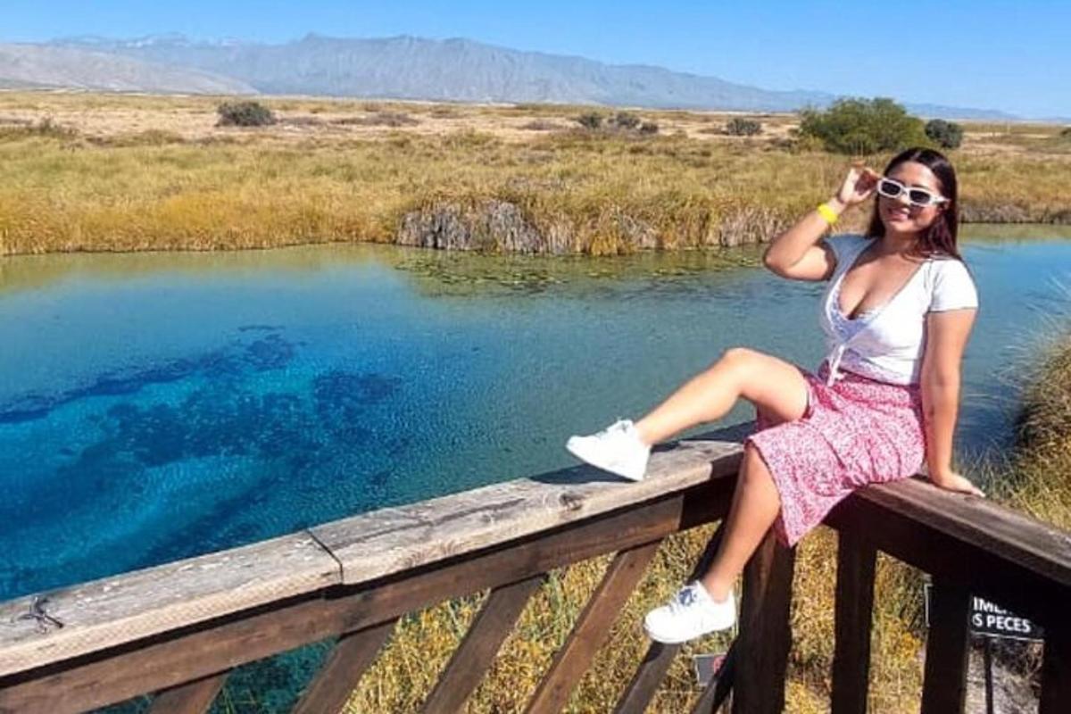 Una mujer sentada en una valla junto a un cuerpo de agua.