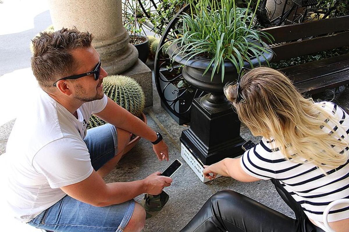 muž a žena sedící na lavičce a dívající se na mobilní telefon