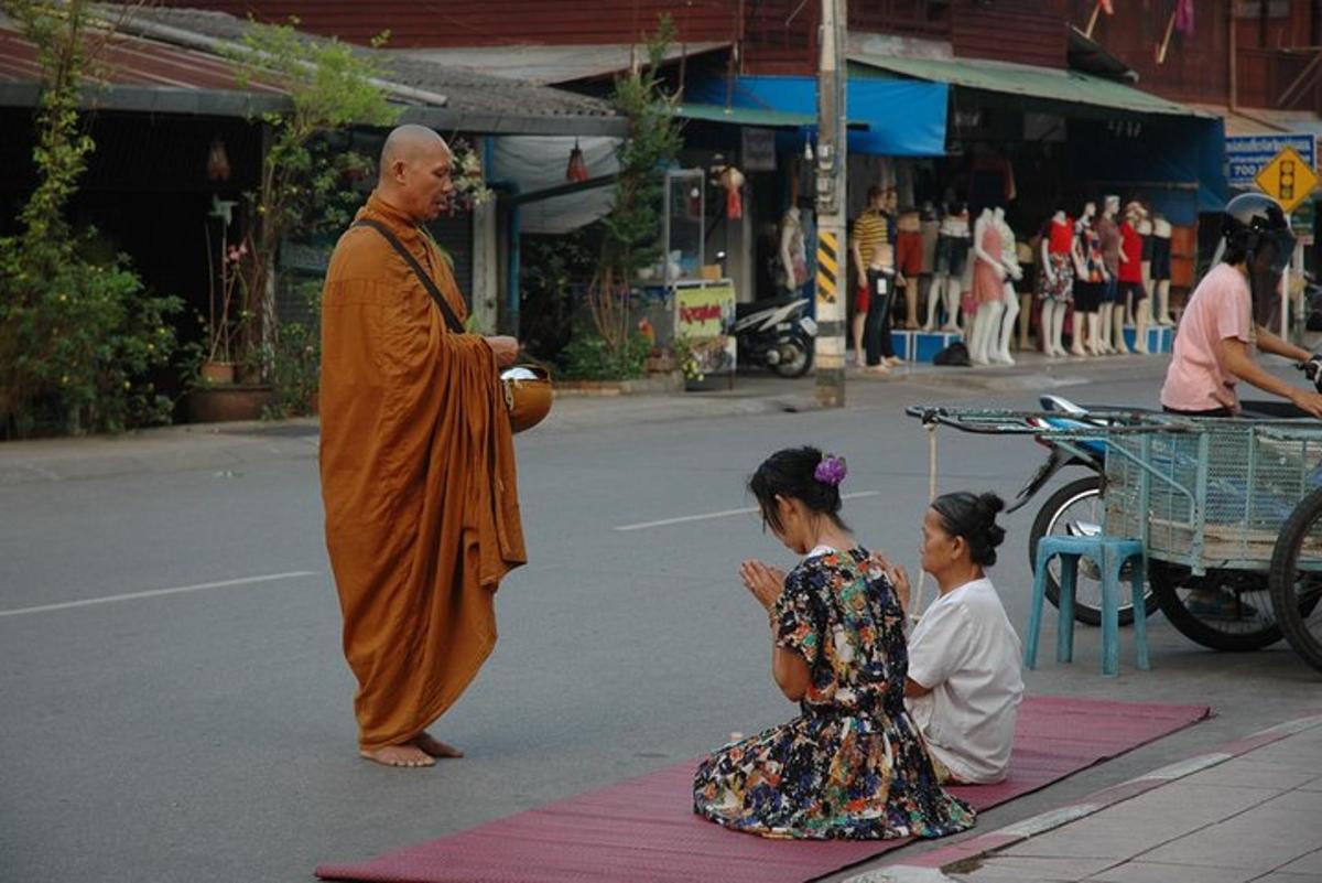 一位僧侣和两个女孩坐在街边的地毯上