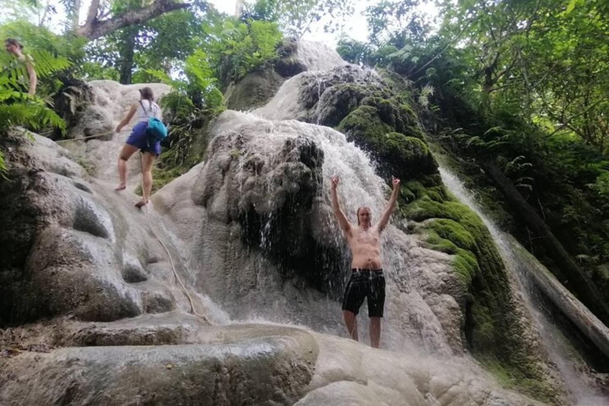 dua orang berdiri di atas batu di air terjun
