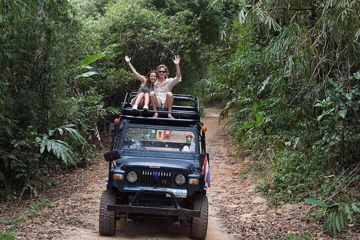 two people sitting on top of a jeep on a dirt road