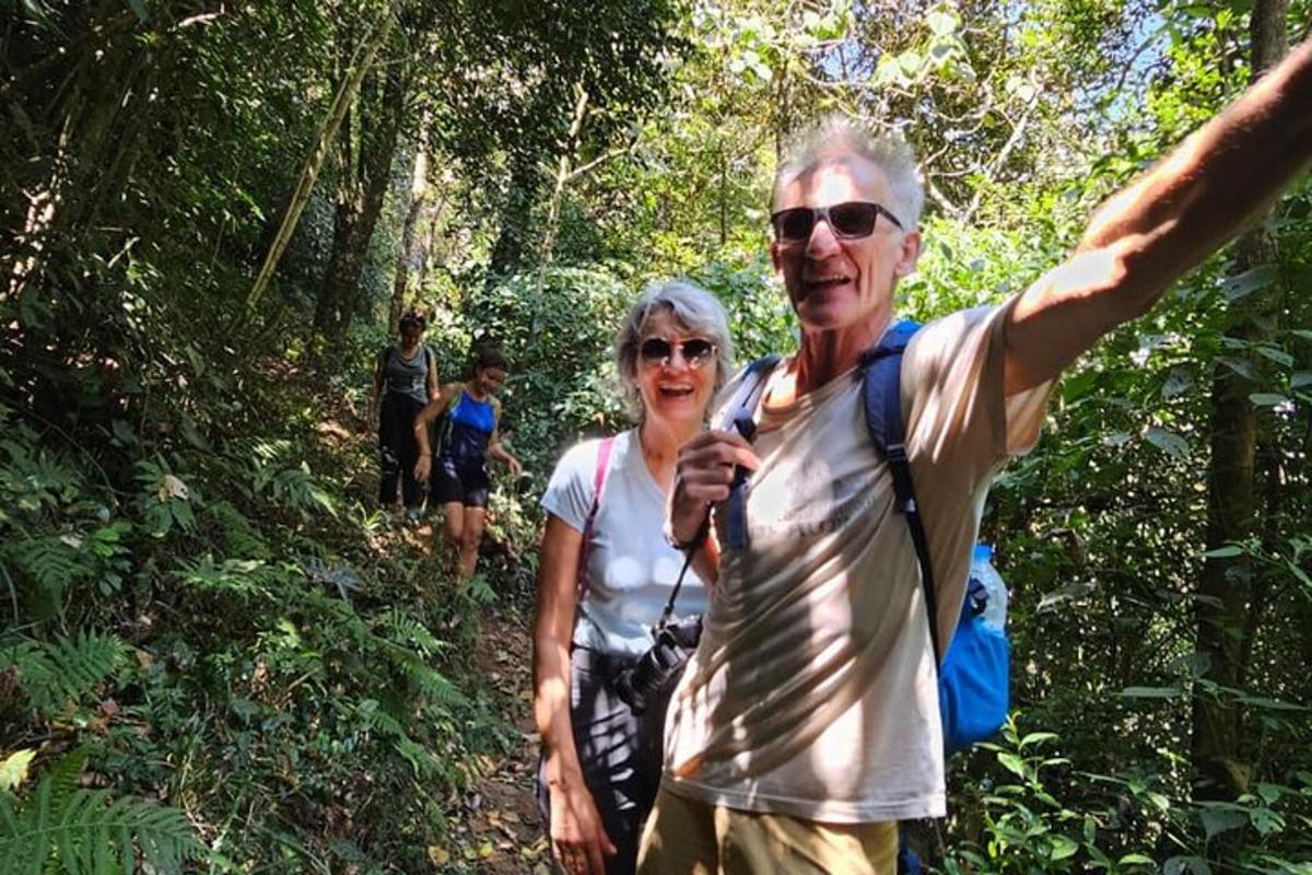 an older man and woman walking on a trail in the woods