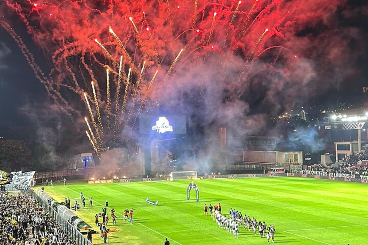 Un campo de fútbol con fuegos artificiales al fondo con una multitud.
