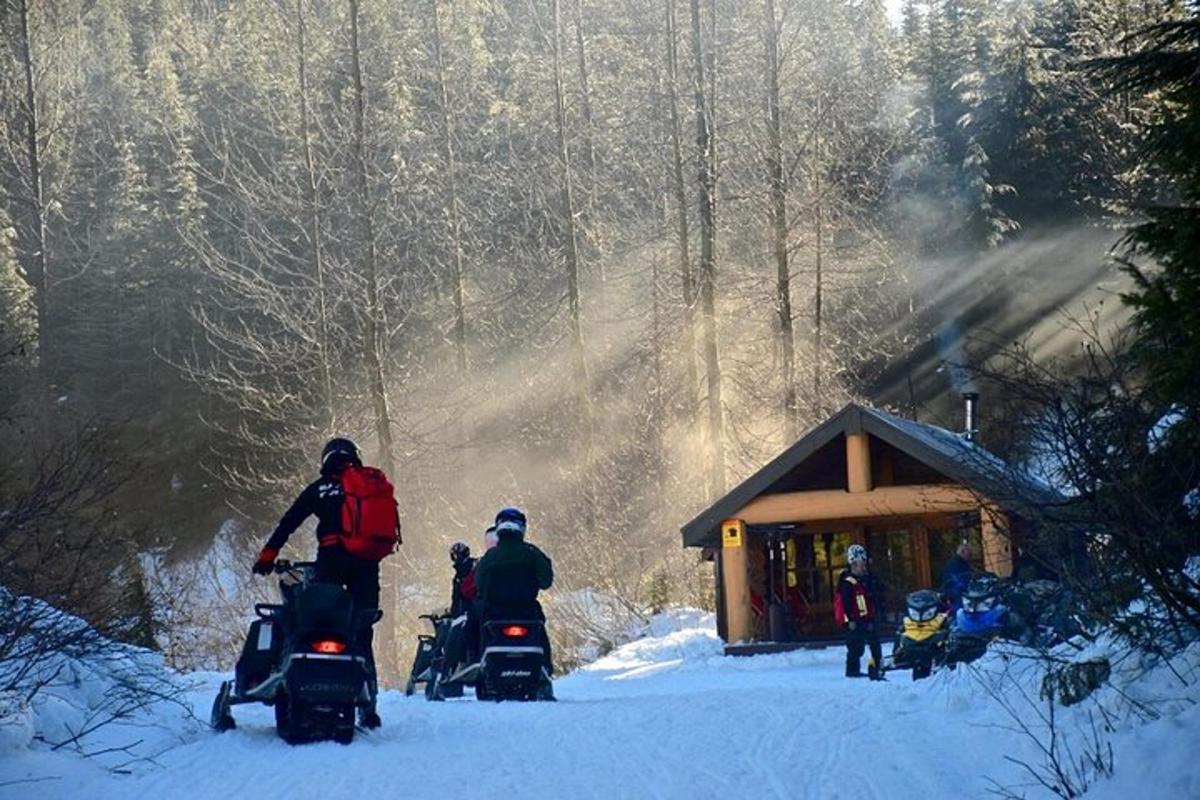 un gruppo di persone su motoslitte nella neve vicino a una baita