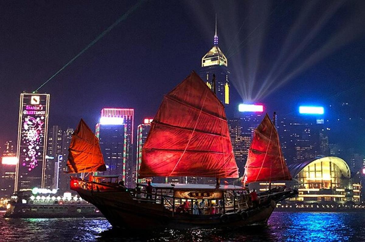 a boat with red sails in the water with a city at night