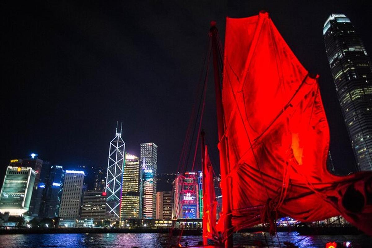a red sail boat in front of a city at night