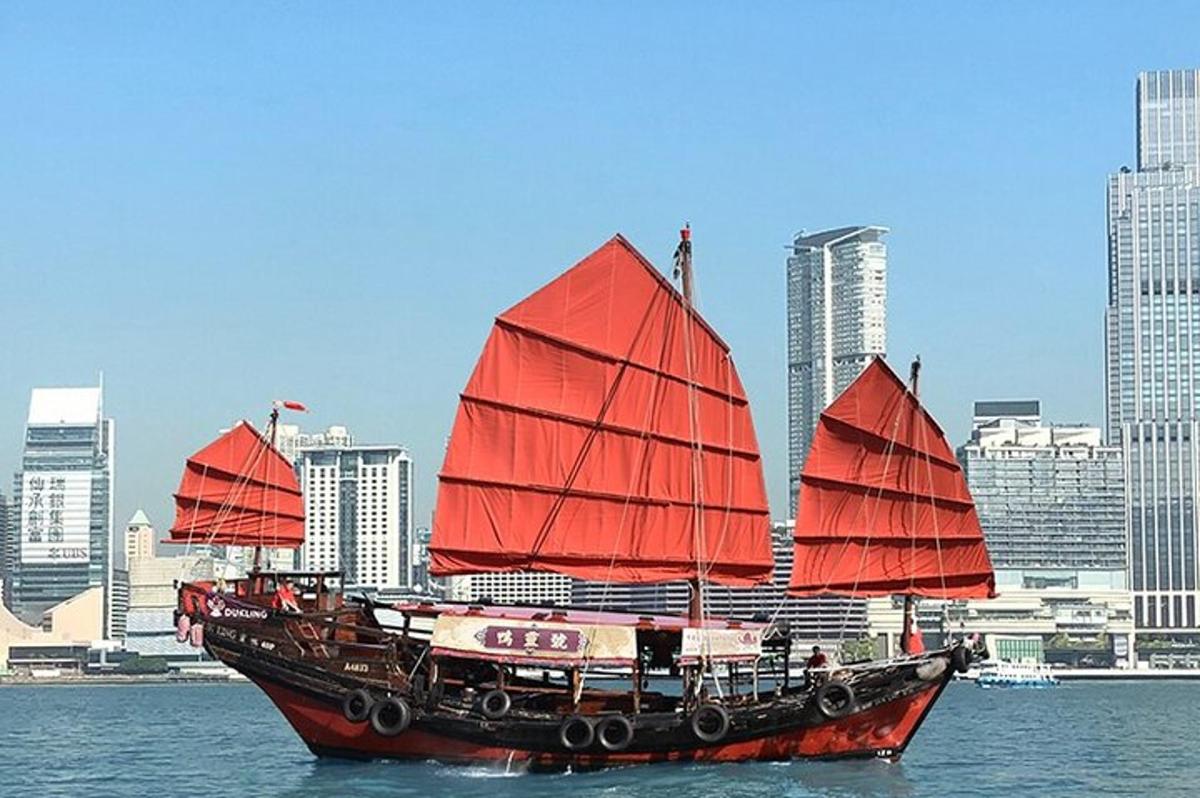 a boat with red sails in the water with a city