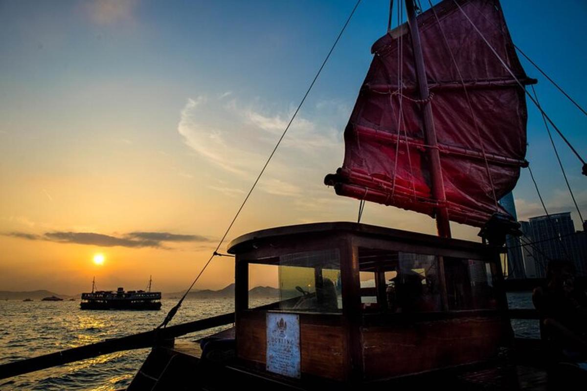 a boat with a red sail on the water at sunset
