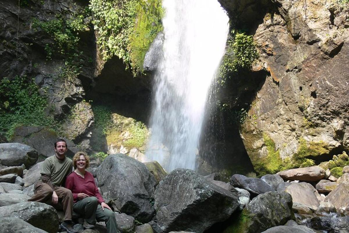 a man and woman sitting on rocks in front of a waterfall