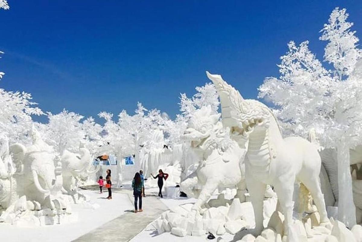 a snow sculpture of horses and trees with people walking around