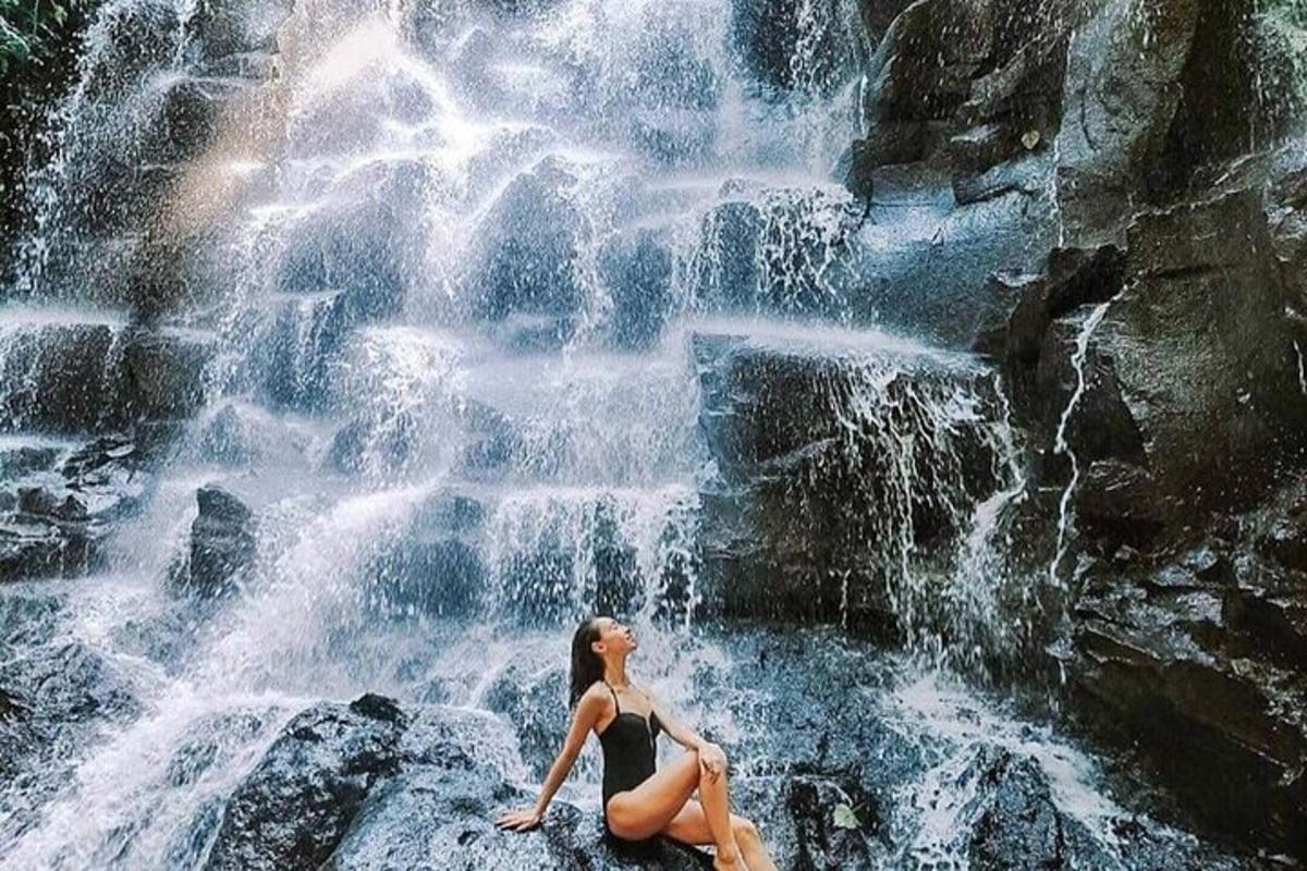 a woman sitting on a rock in front of a waterfall