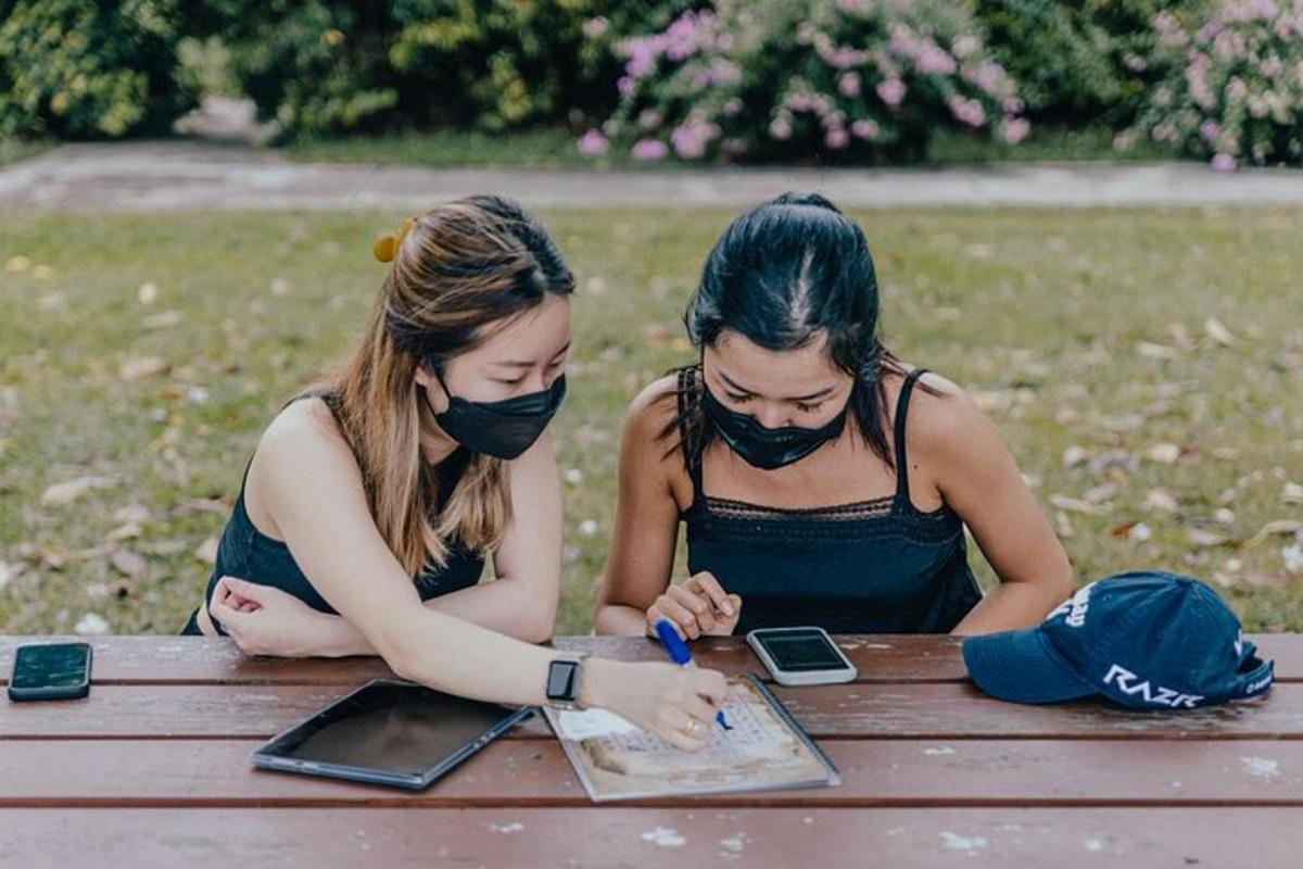 dve dekleti z maskami sedita za mizo za piknik