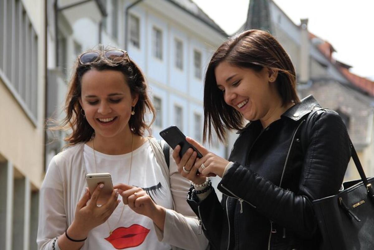две жене се смеју док гледају у своје мобилне телефоне
