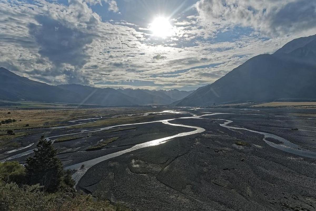 a river in the middle of a valley with the sun