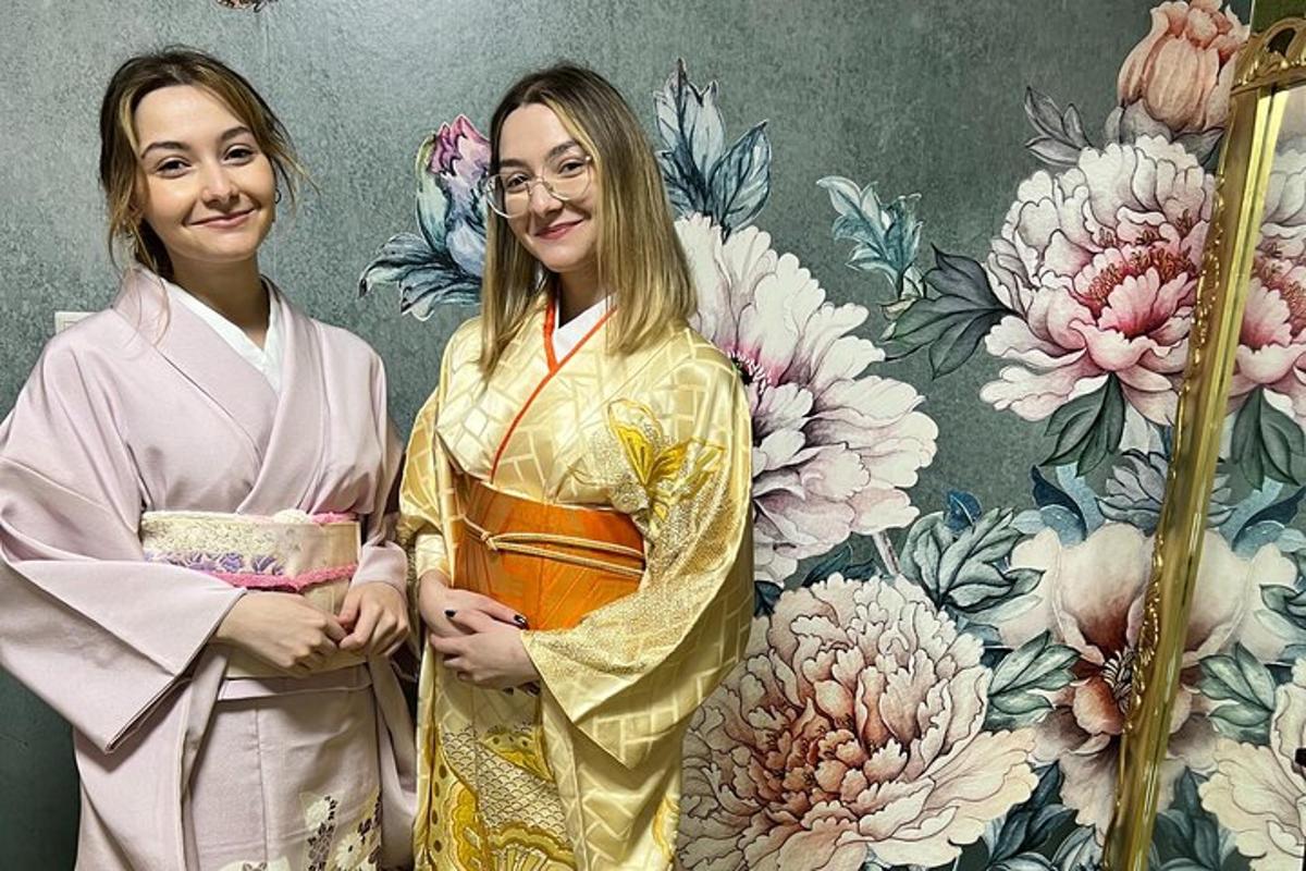 Dvě ženy v kimonech stojící před zdí s květinami