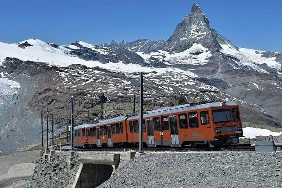 an orange train on the tracks in front of a mountain