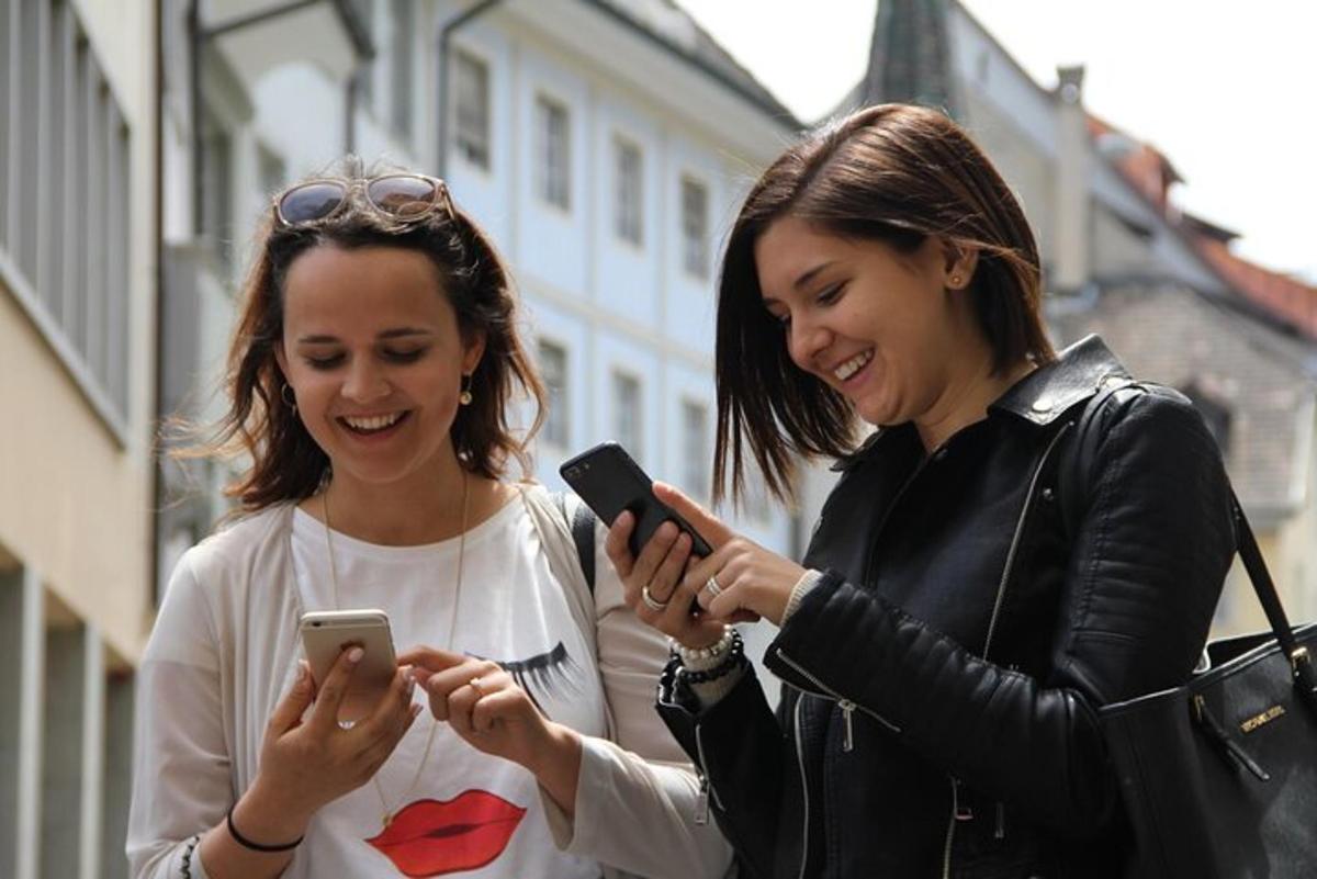 to kvinner som ler mens de ser på mobiltelefonene sine