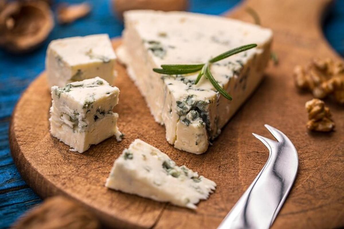 um monte de queijo em um prato de madeira com um garfo e uma faca