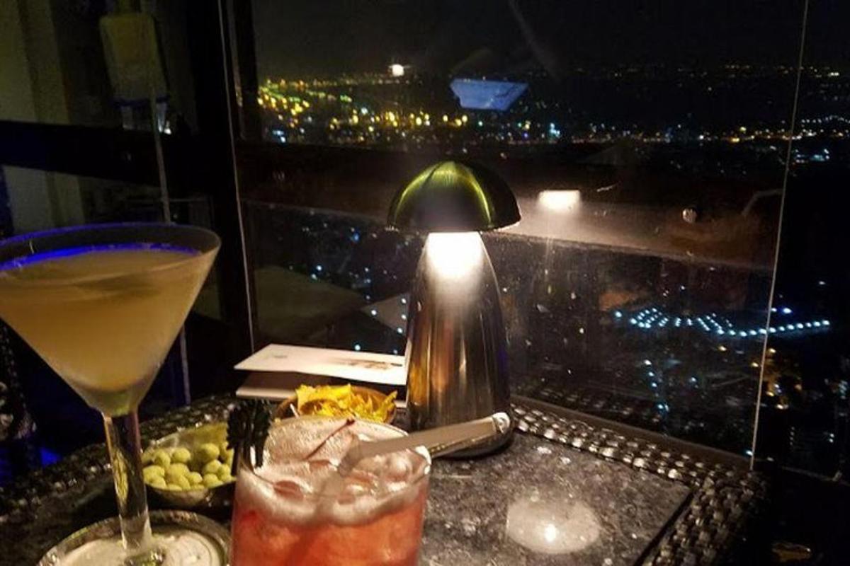 uma mesa com duas bebidas, um abajur e uma janela