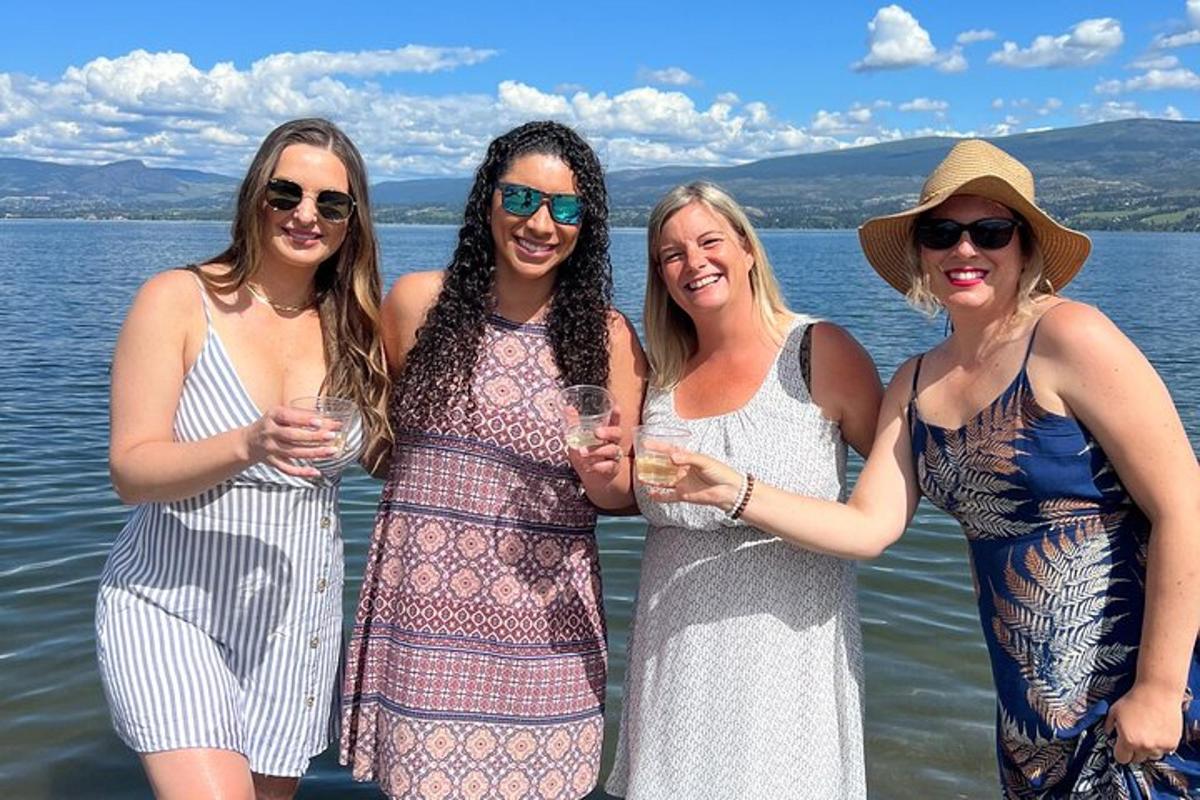 four women standing next to the water holding wine glasses