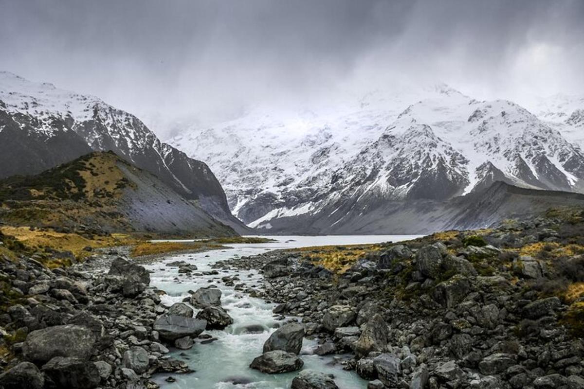 a mountain range with a river and snow covered mountains