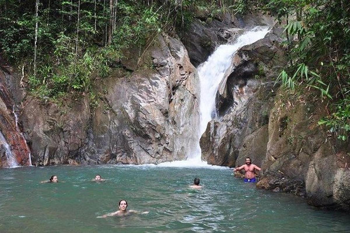 a group of people in the water in front of a waterfall