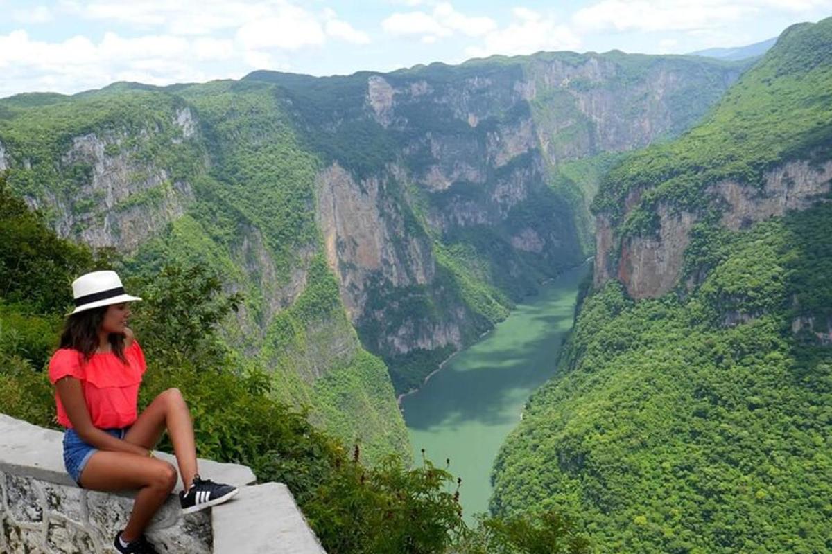 a woman sitting on the edge of a cliff overlooking a river