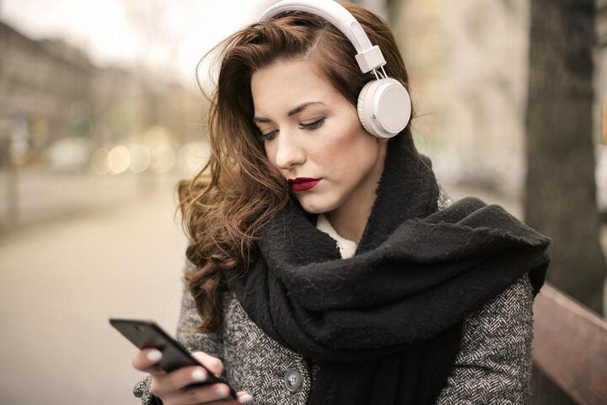 žena se sluchátky a dívá se na svůj mobilní telefon