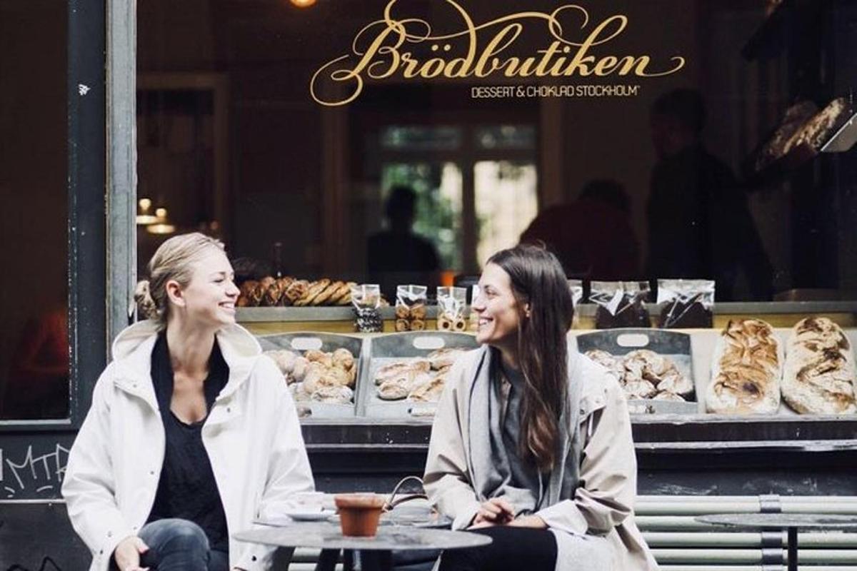 two women sitting on a bench in front of a bakery
